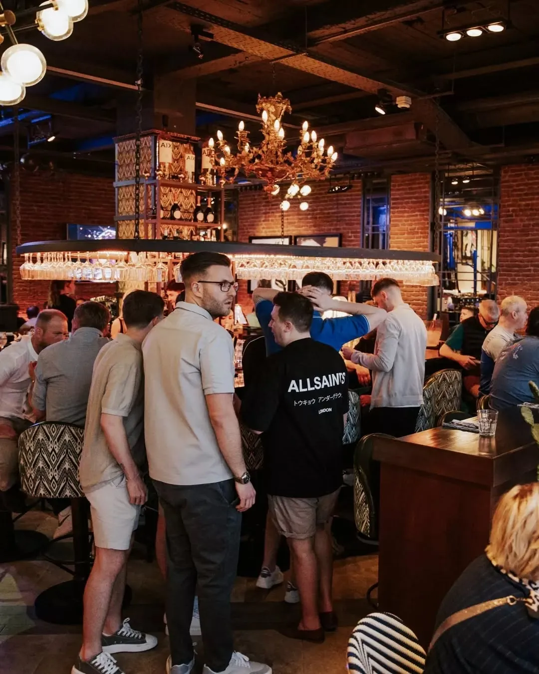 A crowded bar at Jack's with brick walls and a gold chandelier