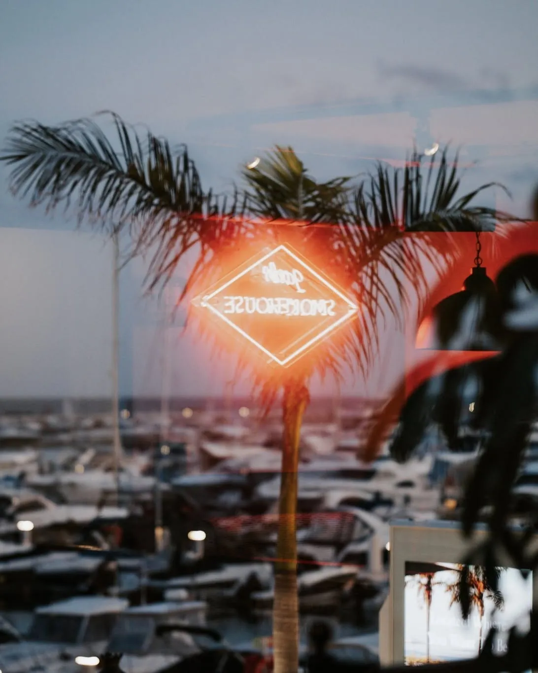 The neon Jack's Smokehouse sign reflected in the window against a sunset over the marina