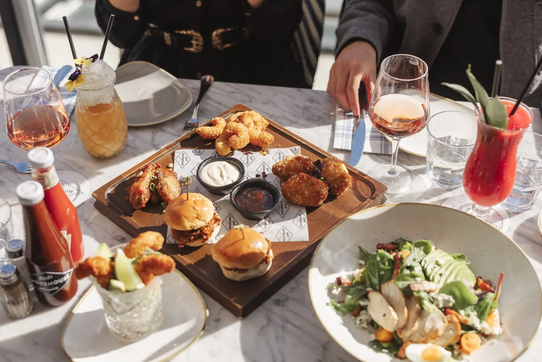 A sunlit marble table at Jack's covered in brunch plates, sliders, wings and cocktails