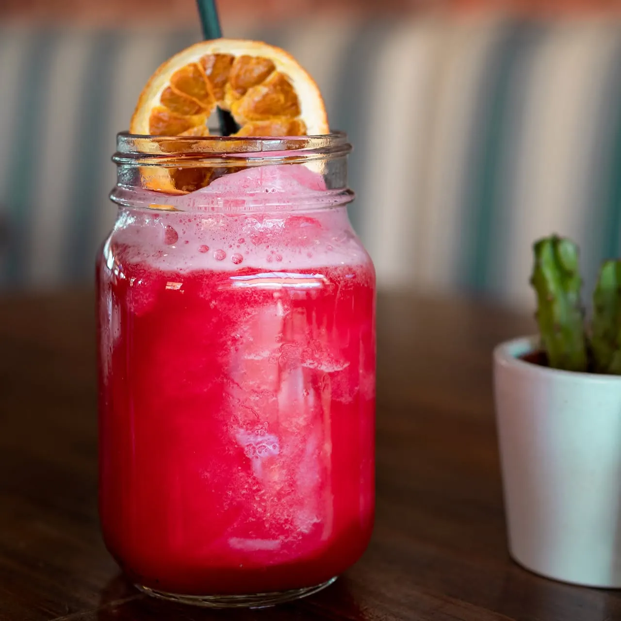 A red cocktail in a mason jar with a dried orange slice