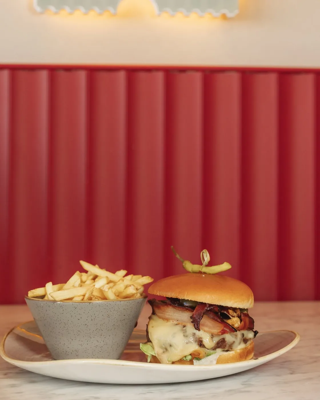 A cheeseburger and fries on a marble table against a red fluted wall