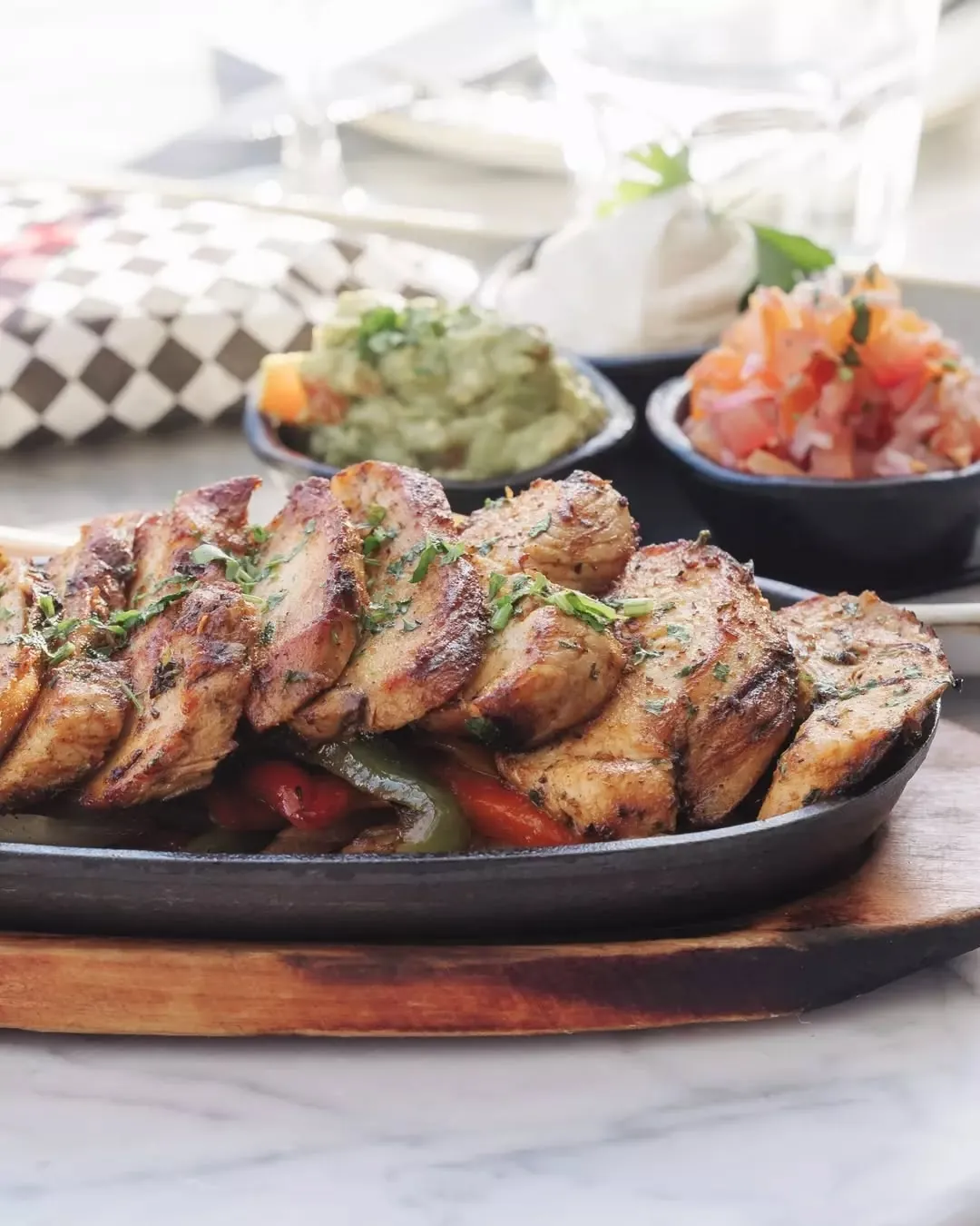 A cast-iron skillet of grilled chicken fajitas with guacamole and pico de gallo