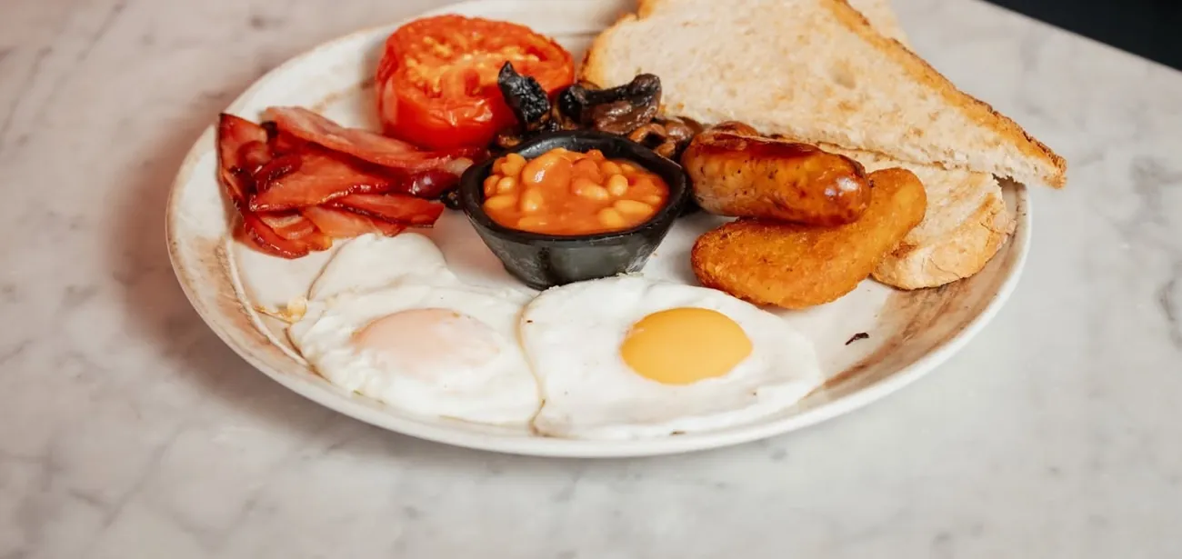 A full English breakfast with eggs, bacon, sausage, beans, hash brown and toast on marble