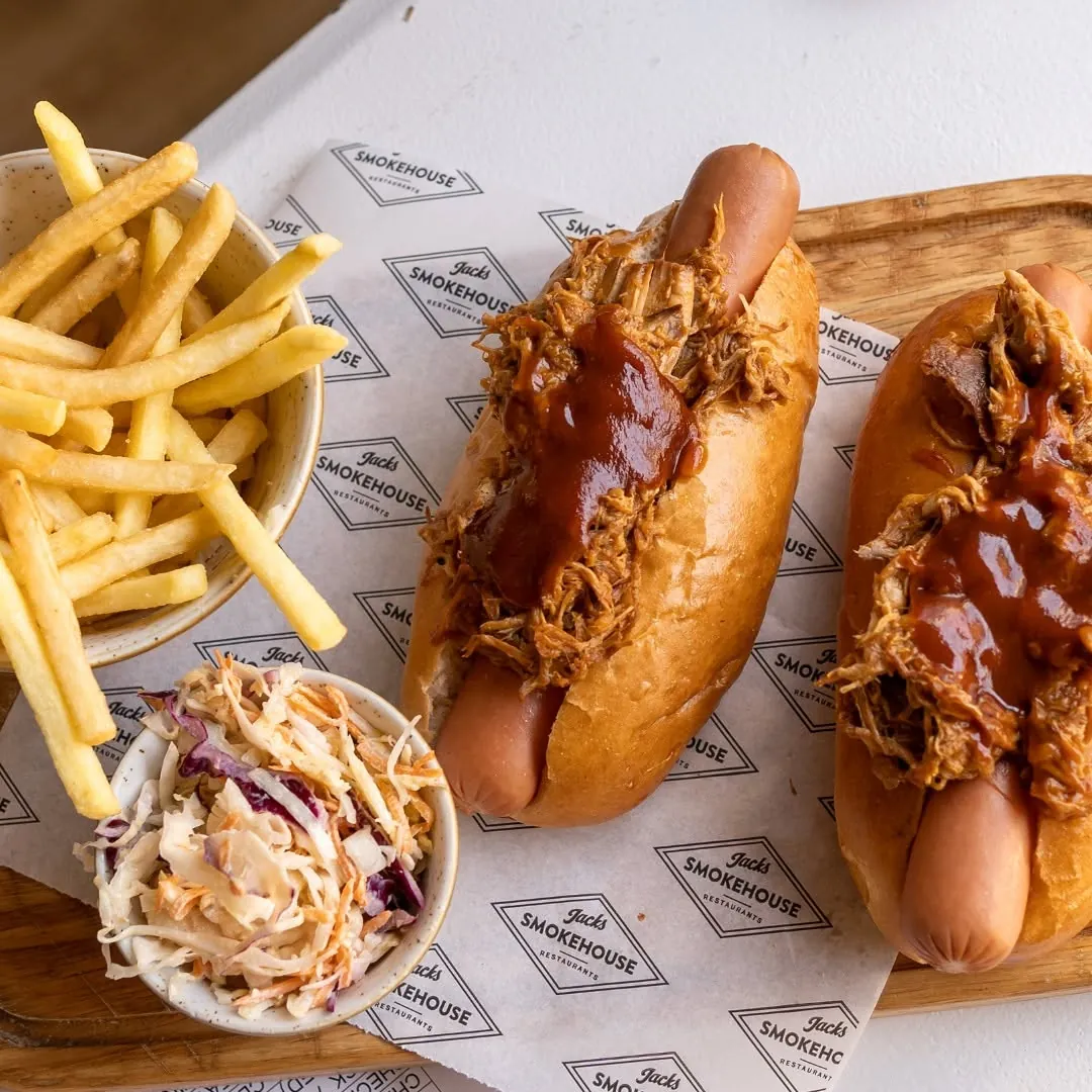 Two pulled pork hot dogs with barbecue sauce on branded Jack's Smokehouse paper