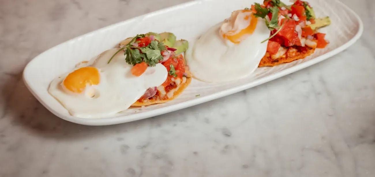 Huevos rancheros with fried eggs, avocado and pico de gallo on a long white plate
