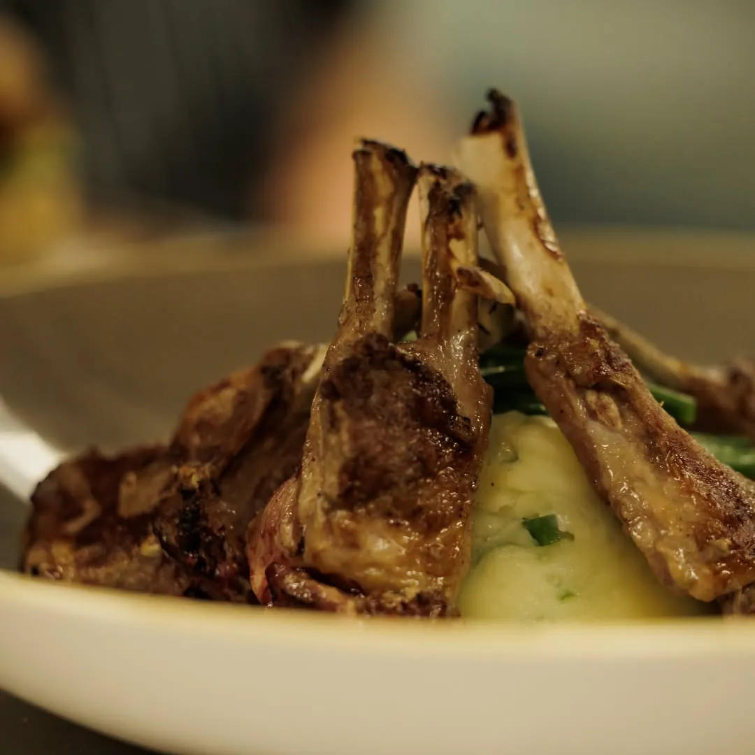 Grilled lamb chops standing in a bowl of mash with green beans