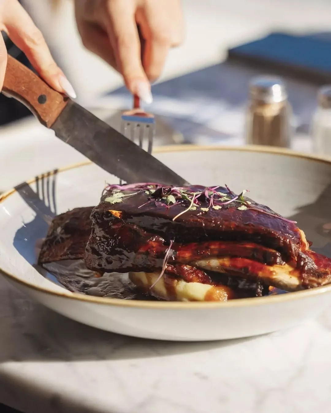A rack of honey barbecue baby back ribs being cut on a gold-rimmed plate