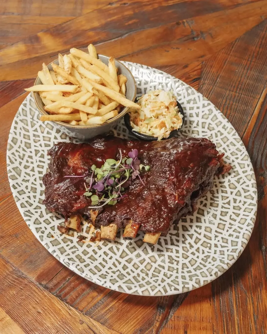 A rack of honey barbecue baby back ribs with fries and slaw on a patterned plate