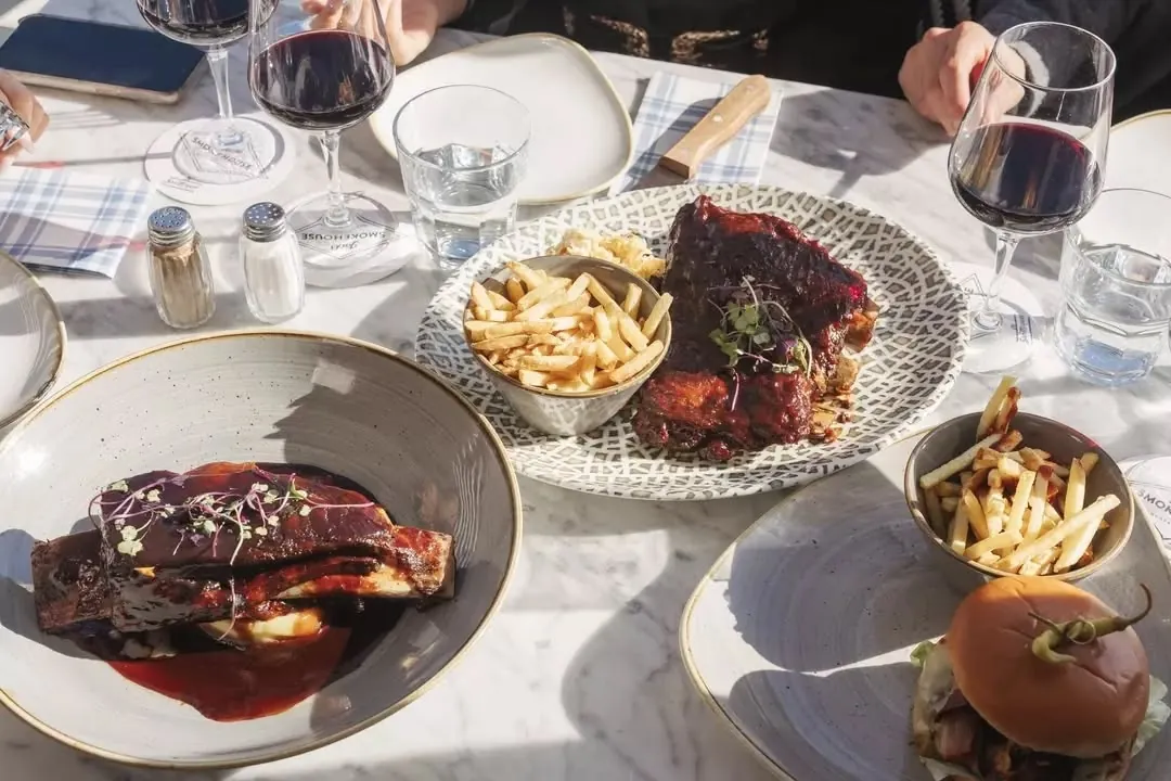 Ribs, a burger and fries on a sunlit marble table with red wine
