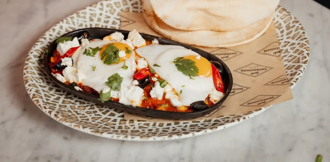 Shakshuka with eggs, feta and olives in a cast-iron dish with pita