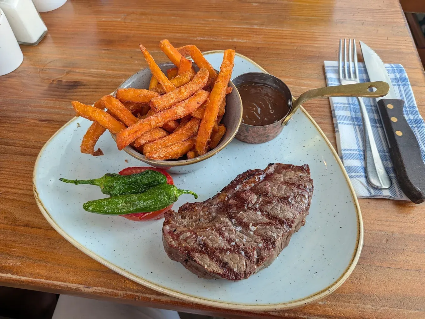 A grilled sirloin steak with sweet potato fries, padron peppers and barbecue sauce