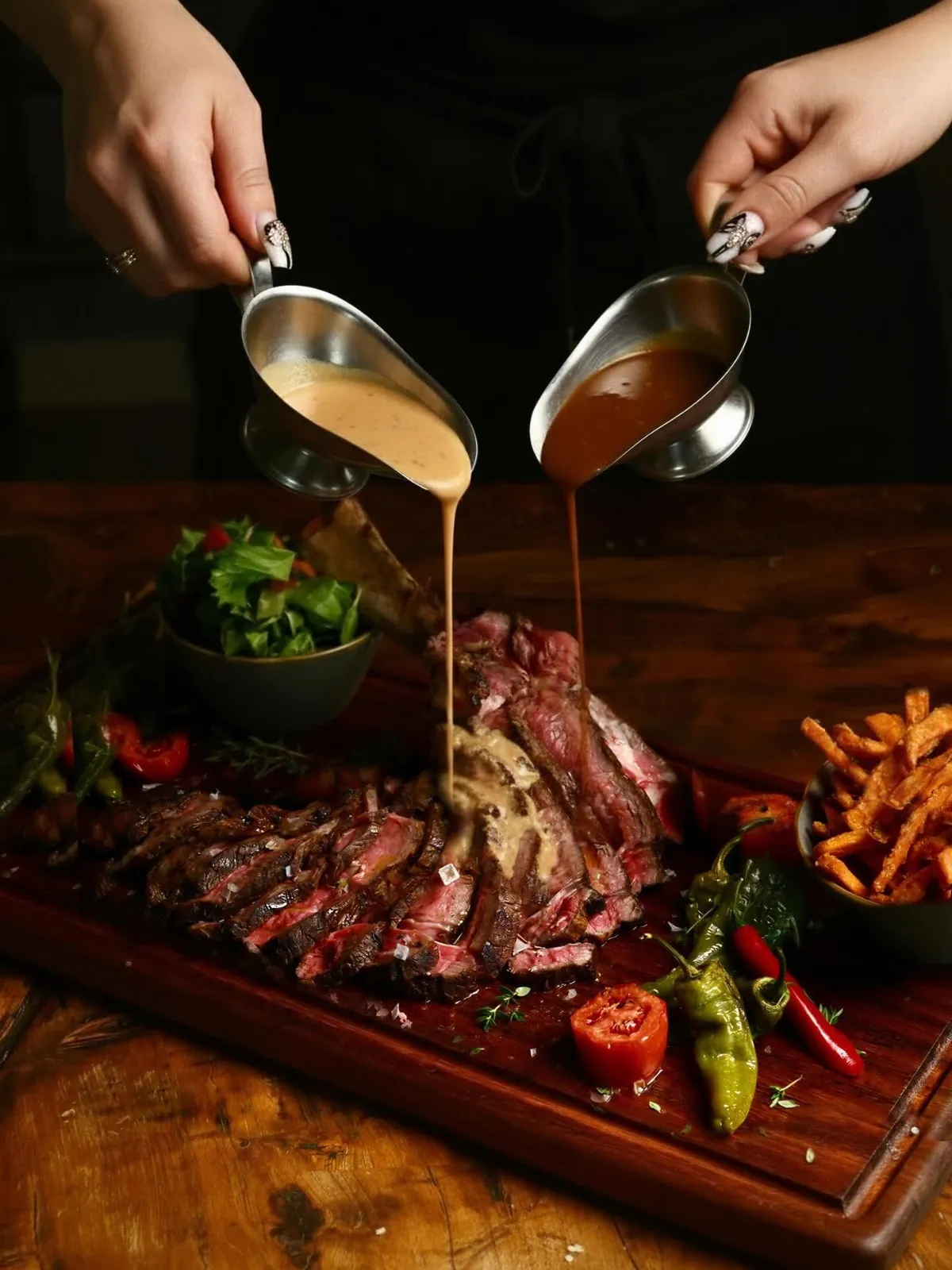 Two jugs of sauce poured over a sliced, bone-in steak on a wooden board