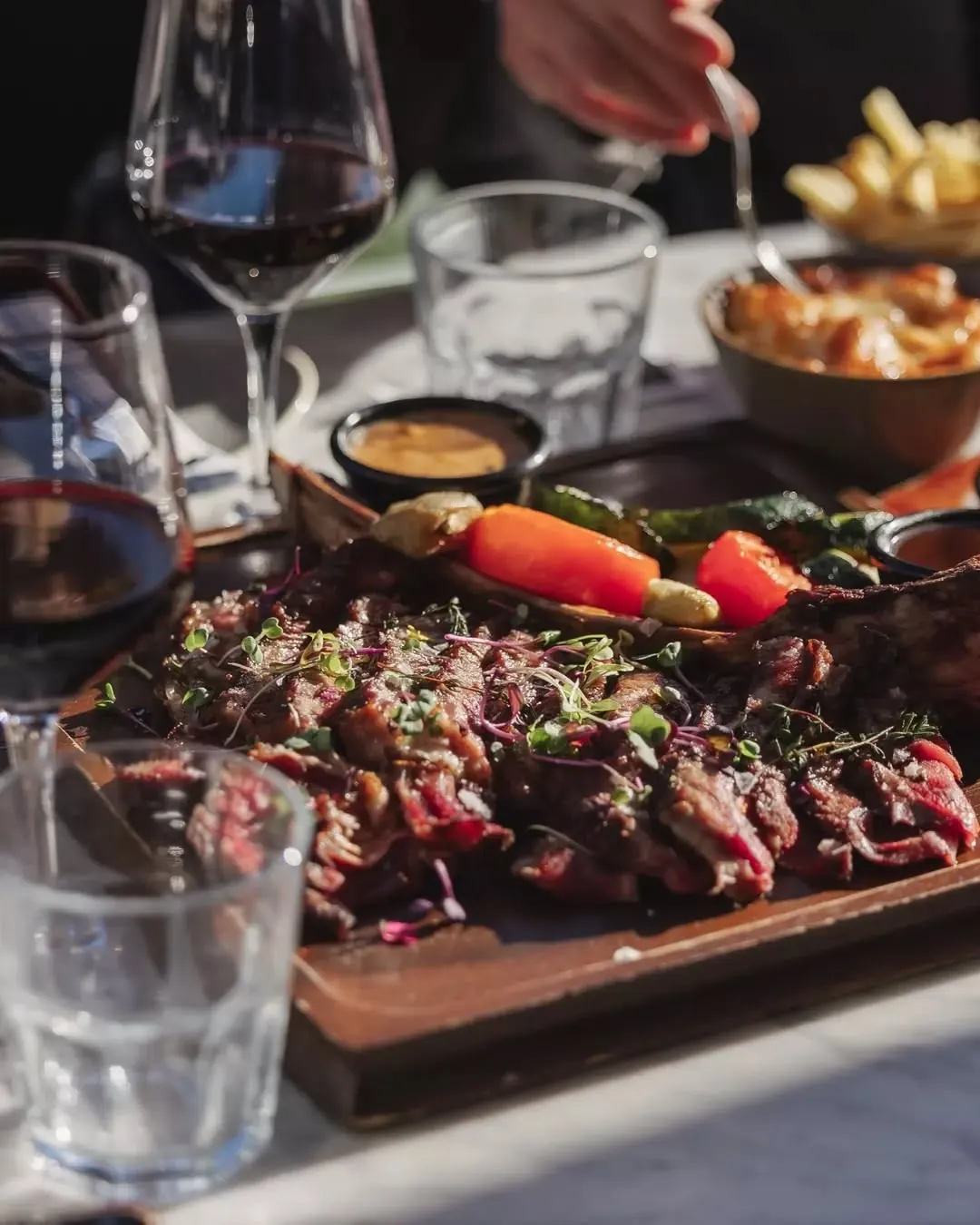 A sliced tomahawk steak on a board in the sun with red wine and mac 'n cheese