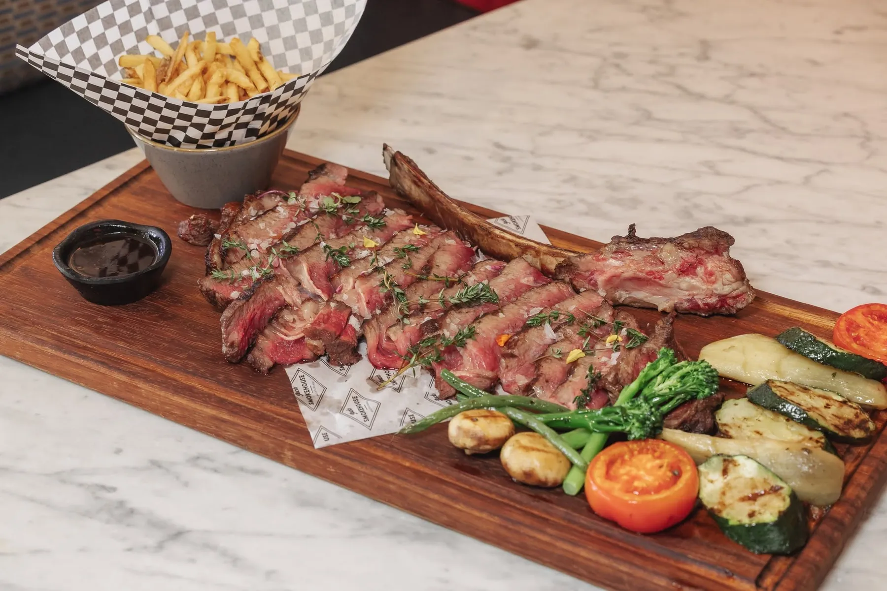 A sliced 40-day dry-aged tomahawk steak on a wooden board with fries and grilled vegetables